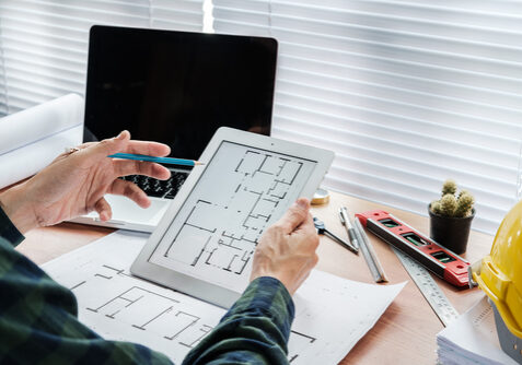 Businessman,Hand,Working,With,Tablet,And,Blueprint,On,Architectural,Project